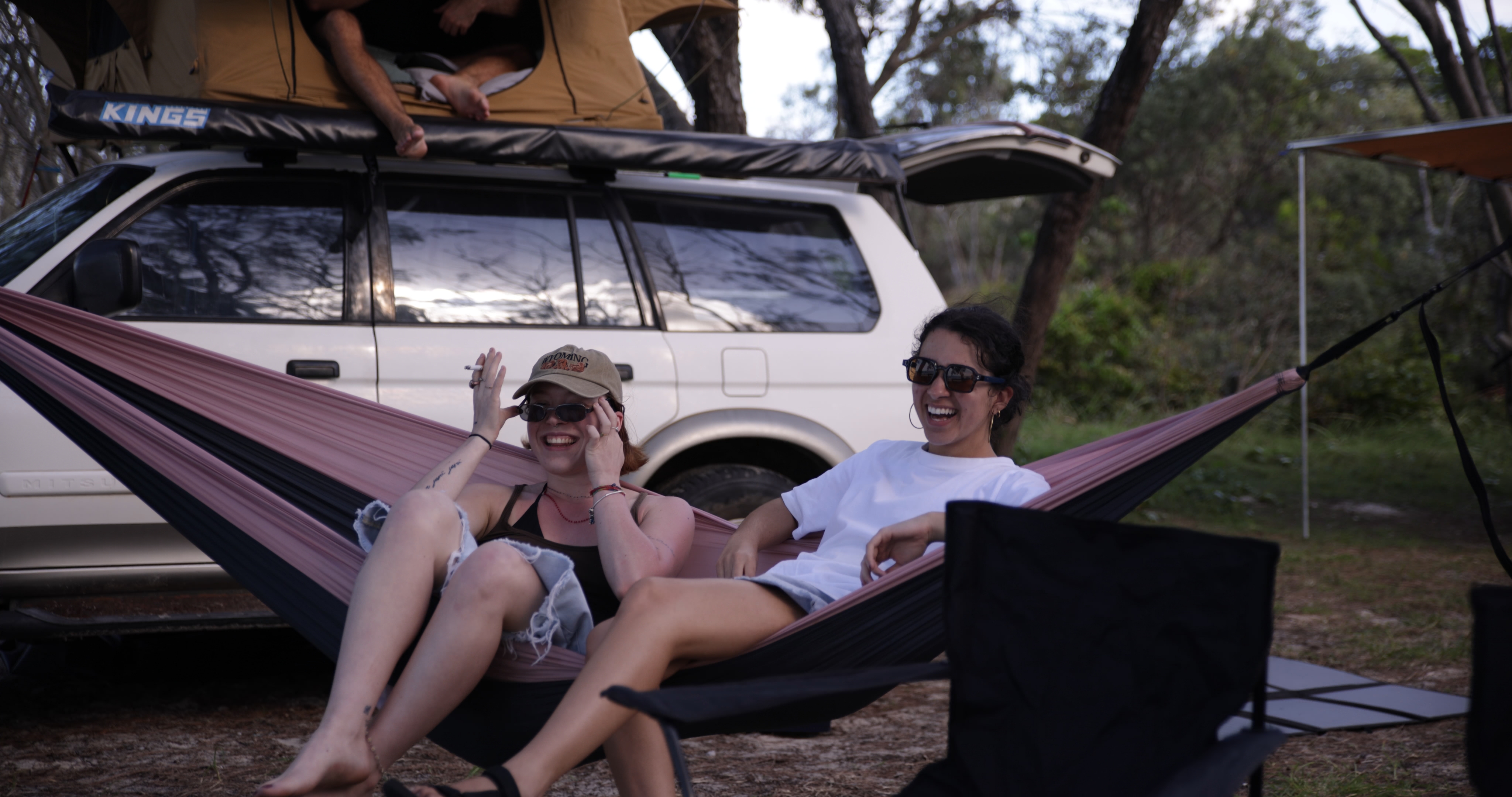 Three people laughing and dancing at a camp table in golden hour with drinks